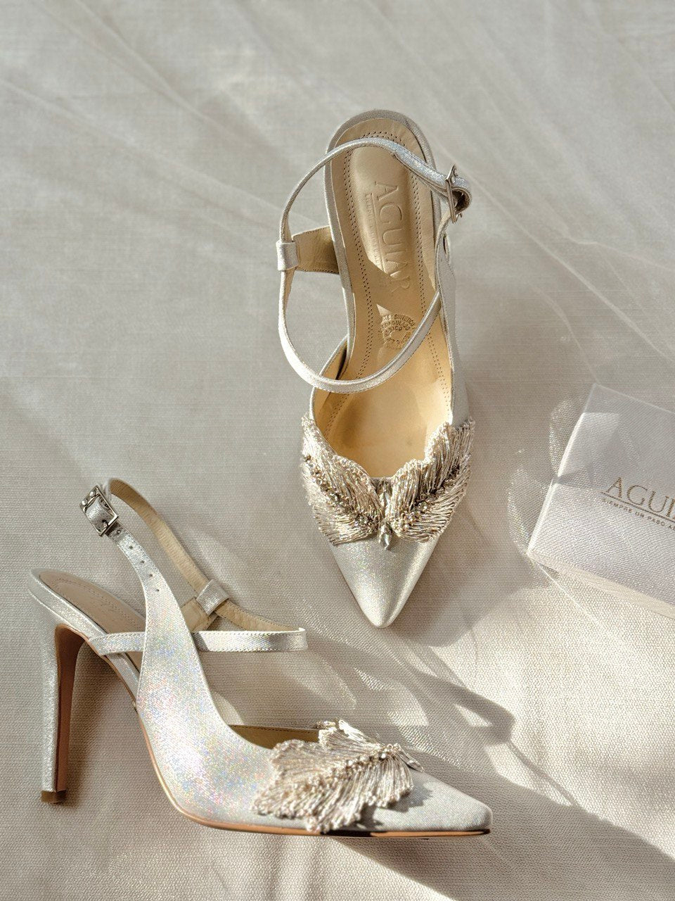 Zapatillas de novia stileto en tono plata con destellos tornasol y aplicacion textil con hilos de plata e incrustacion de cristal navette en el centro